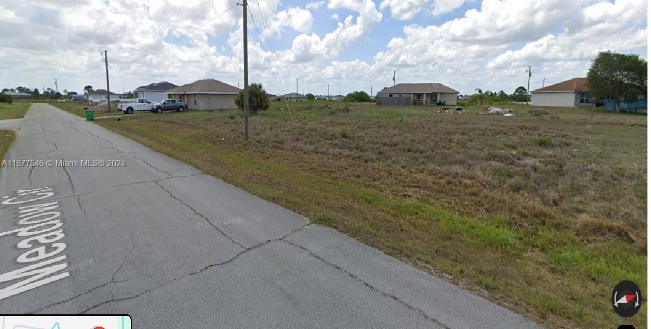 A vacant, grassy residential lot sits next to a paved road with houses nearby — 9036 Meadow Terr, La Belle FL 33935, LA BELLE, FL
