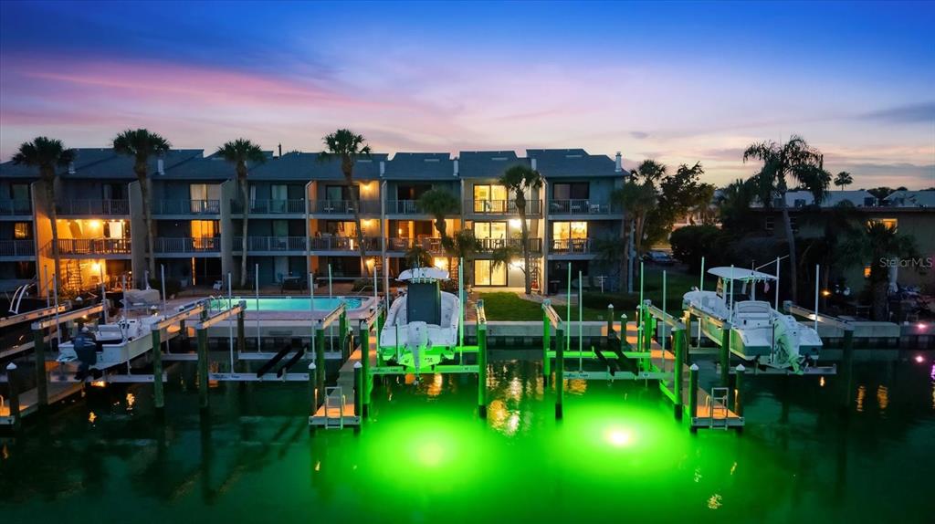 An aerial view shows a multi-story waterfront building with boat slips and green underwater lights — 11835 3RD STREET E, TREASURE ISLAND, FL
