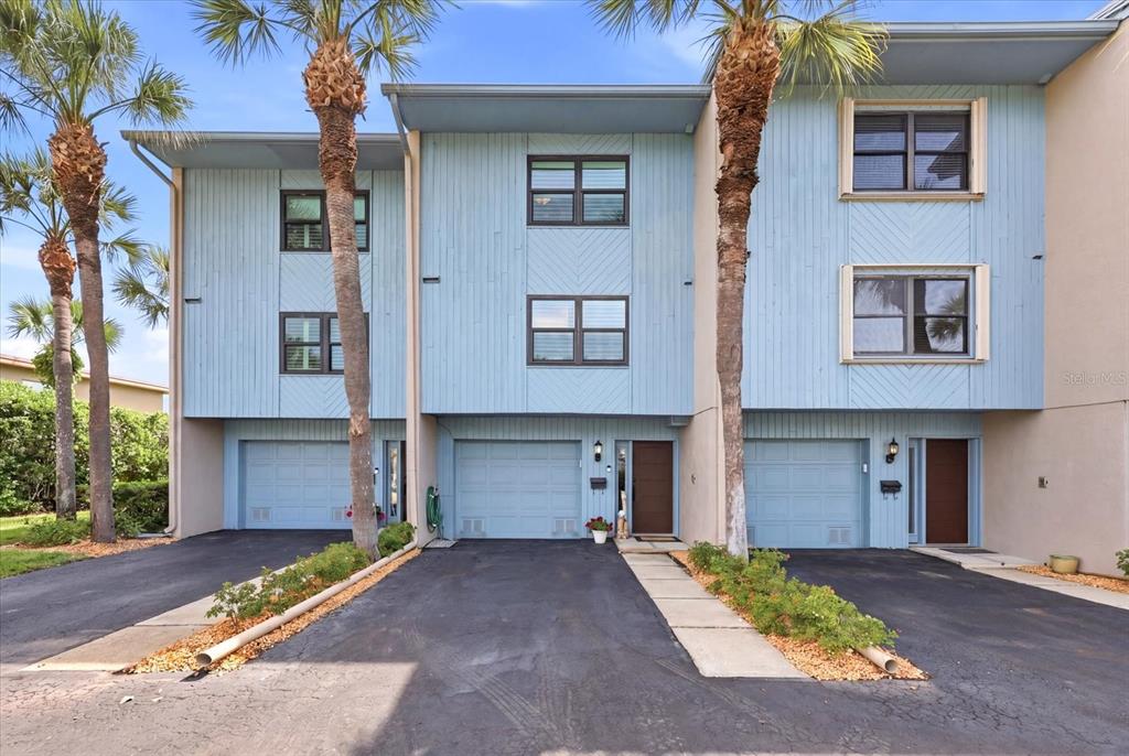 A three-story townhouse exterior with blue vertical siding, attached garages, and palm trees — 11835 3RD STREET E, TREASURE ISLAND, FL