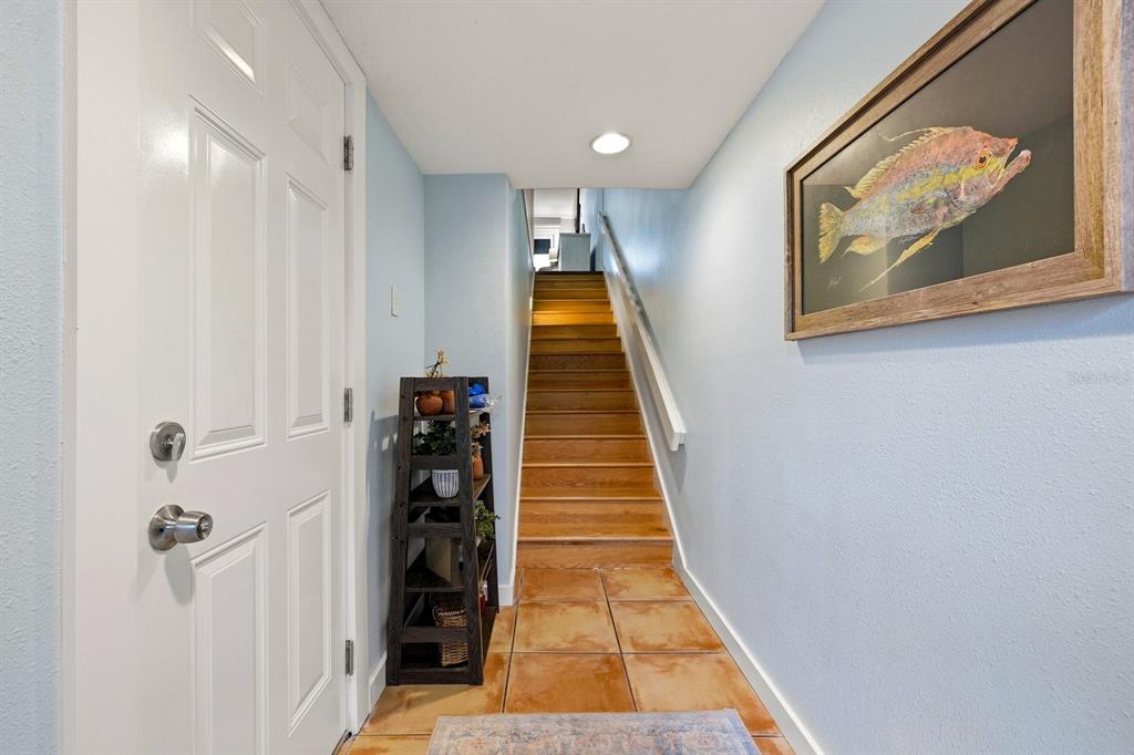 An entryway features a white door, a wooden staircase, tiled flooring, and a framed fish print — 11835 3RD STREET E, TREASURE ISLAND, FL