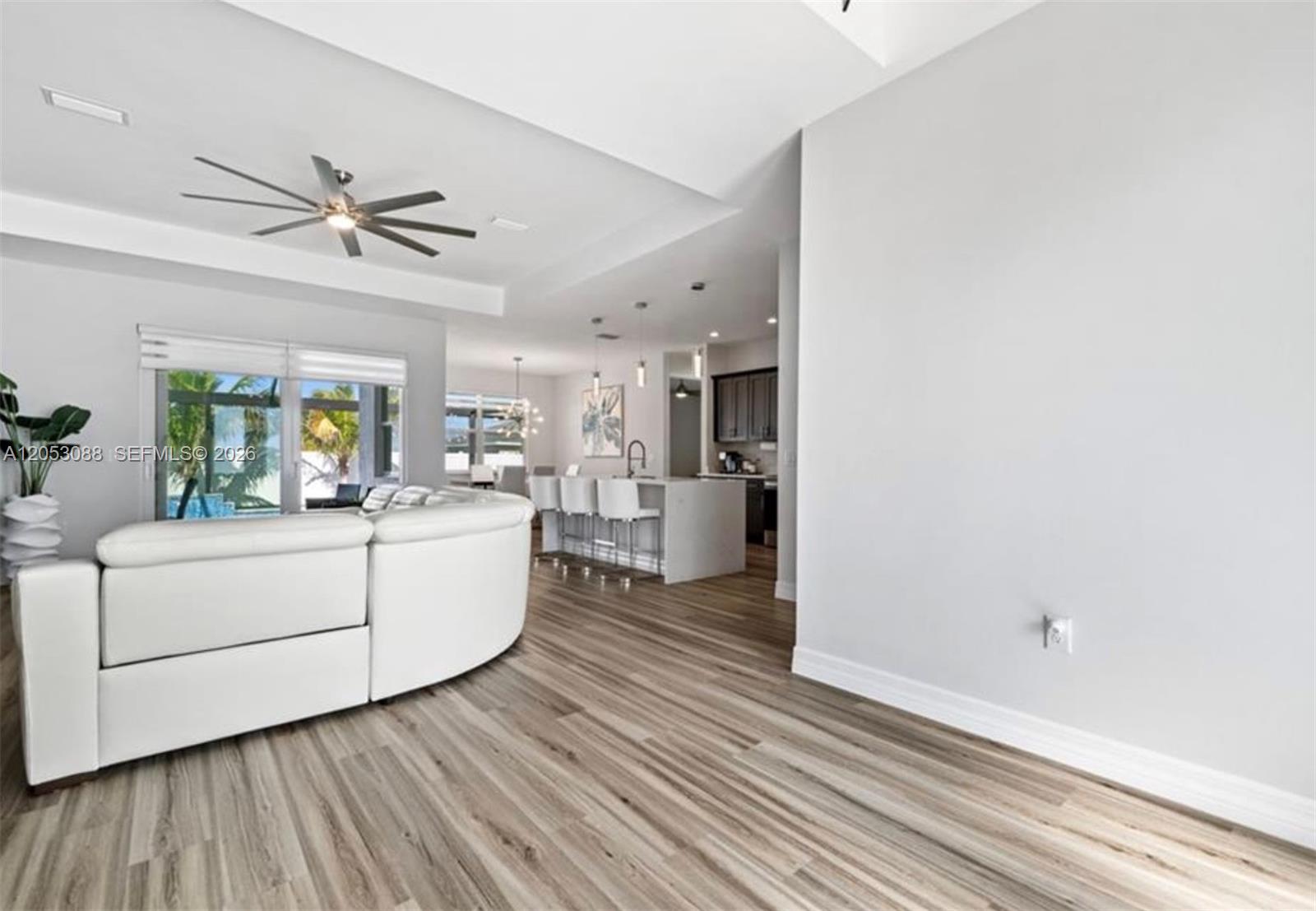 A living room with a white curved sofa, wood-look flooring, and an open kitchen island — 1017 NW 15th ter, Cape Coral FL 33993, CAPE CORAL, FL