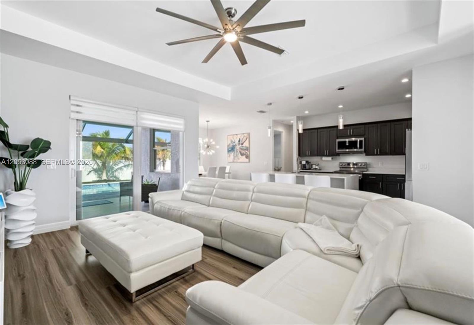 A white sectional sofa and ottoman sit in a living room with wood-look flooring — 1017 NW 15th ter, Cape Coral FL 33993, CAPE CORAL, FL