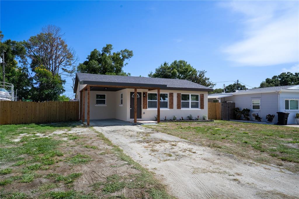 A single-story house with a carport, tan stucco exterior, and a dirt driveway — 5460 77TH AVENUE N, PINELLAS PARK, FL