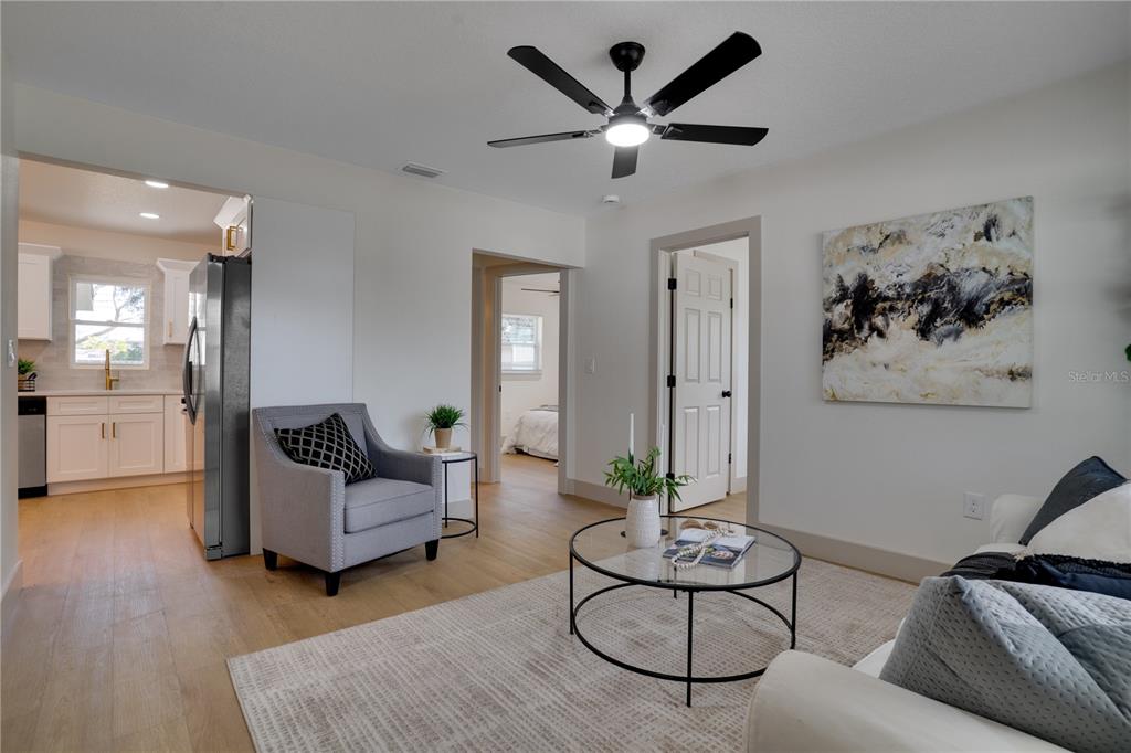 A living room with light wood floors, a ceiling fan, and a view into the kitchen — 5460 77TH AVENUE N, PINELLAS PARK, FL