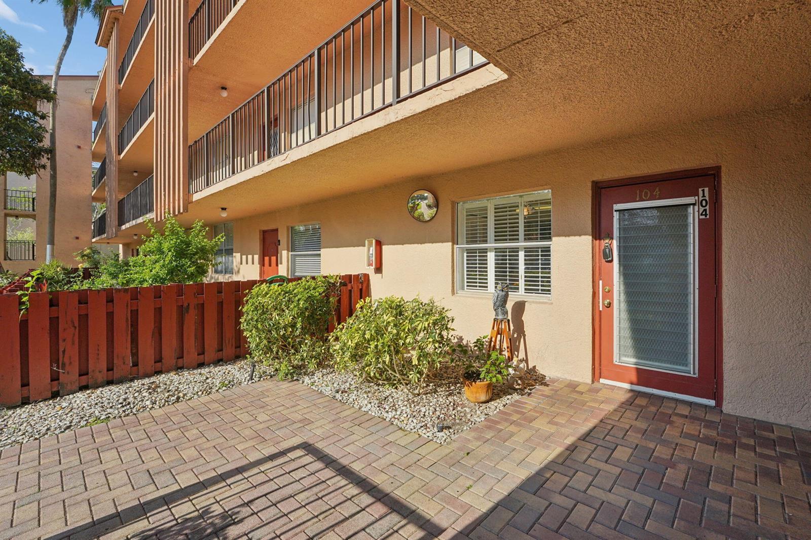 A ground-level apartment entrance features a red door, brick patio, and a small garden — 370 NW 76th Avenue # 104, Margate FL 33063, MARGATE, FL