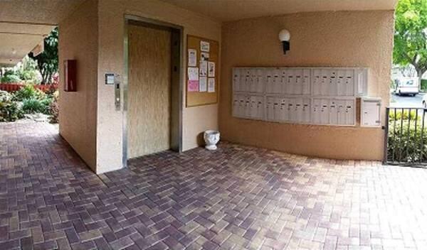 An outdoor covered entryway features brick pavers, a wooden elevator door, and a wall-mounted mailbox unit — 370 NW 76th Avenue # 104, Margate FL 33063, MARGATE, FL