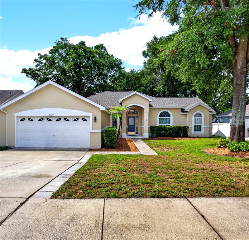 A single-story house with a two-car garage, beige stucco exterior, and a front walkway — 2689 SUNBURY ST, CLERMONT, FL