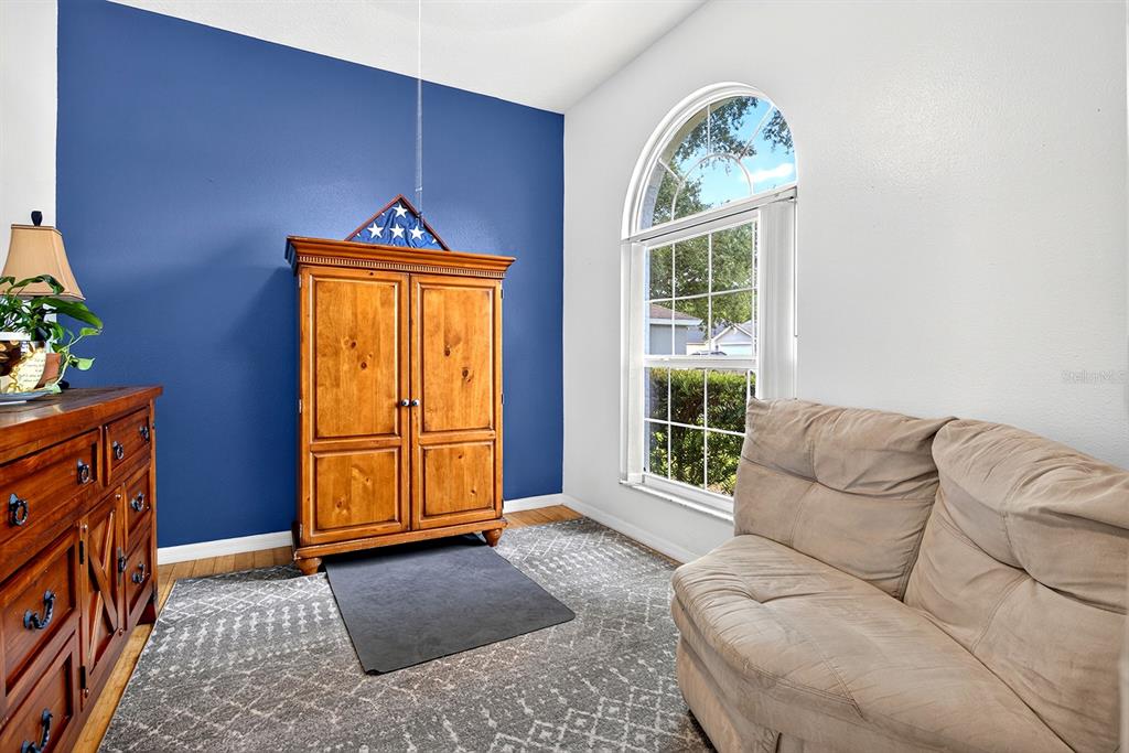 A room with a blue accent wall, wooden armoire, arched window, and beige loveseat — 2689 SUNBURY ST, CLERMONT, FL