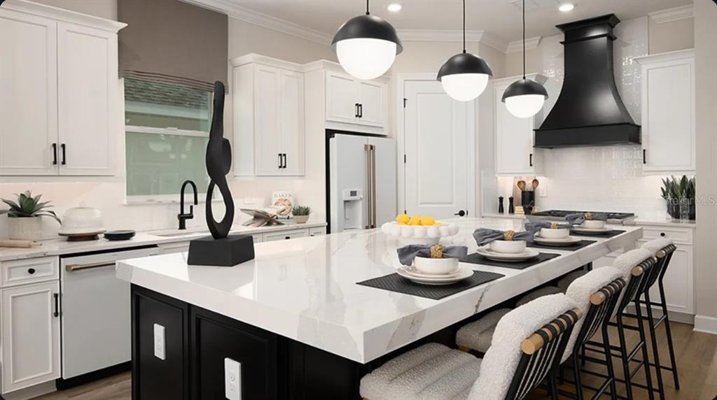 A modern kitchen features white cabinetry, a large marble-topped island, and a black range hood — 11192 CARDING MILL LANE, WINTER GARDEN, FL