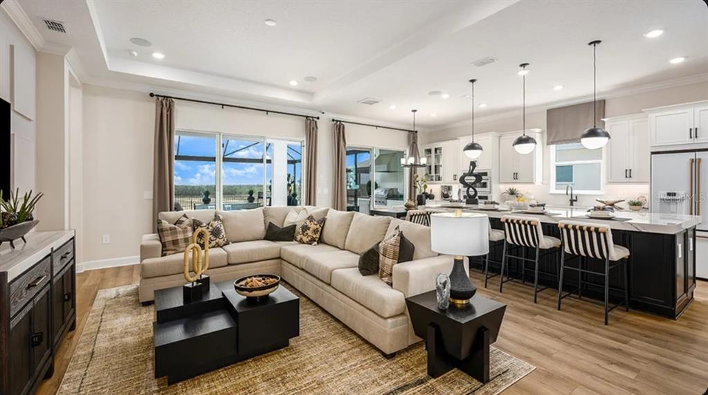 An open-concept living room and kitchen feature a sectional sofa, island seating, and wood flooring — 11192 CARDING MILL LANE, WINTER GARDEN, FL