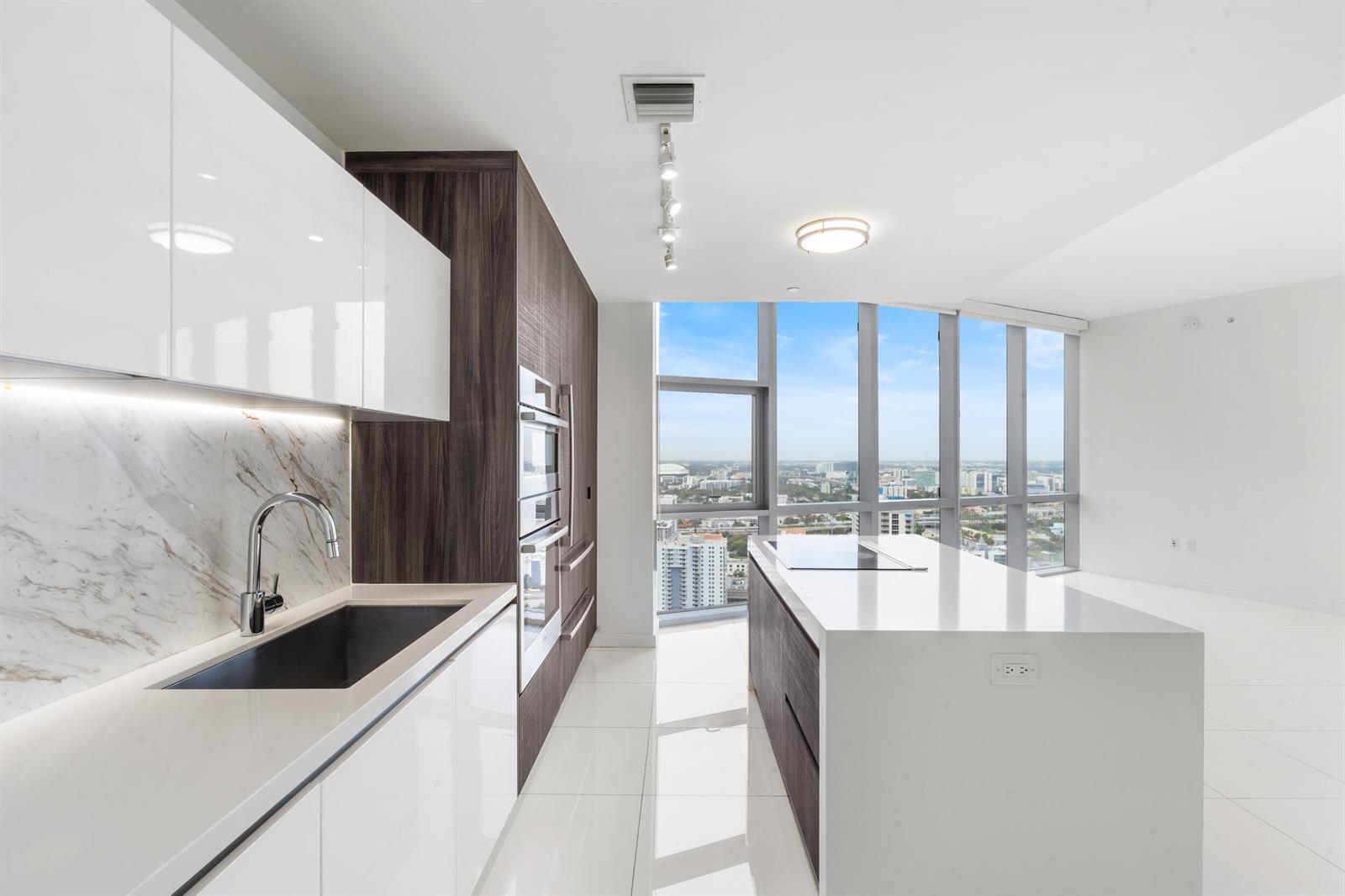 A modern kitchen features white glossy cabinets, dark wood accents, a marble backsplash, and floor-to-ceiling windows — 851 NE 1st Avenue # 3202, Miami FL 33130, MIAMI, FL
