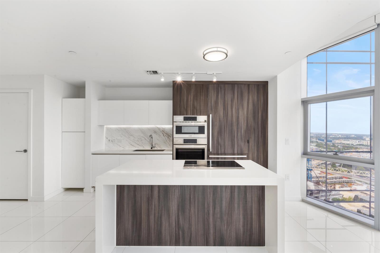 A modern kitchen features a white island, dark wood cabinetry, and floor-to-ceiling windows — 851 NE 1st Avenue # 3202, Miami FL 33130, MIAMI, FL