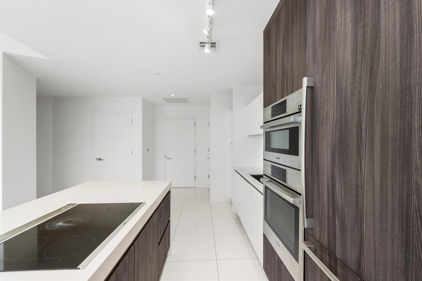 A modern kitchen features dark wood cabinetry, white countertops, a cooktop island, and built-in appliances — 851 NE 1st Avenue # 3202, Miami FL 33130, MIAMI, FL