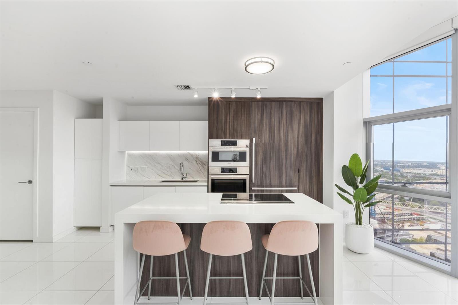 A modern kitchen features a white island with pink stools, dark wood cabinetry, and floor-to-ceiling windows — 851 NE 1st Avenue # 3202, Miami FL 33130, MIAMI, FL