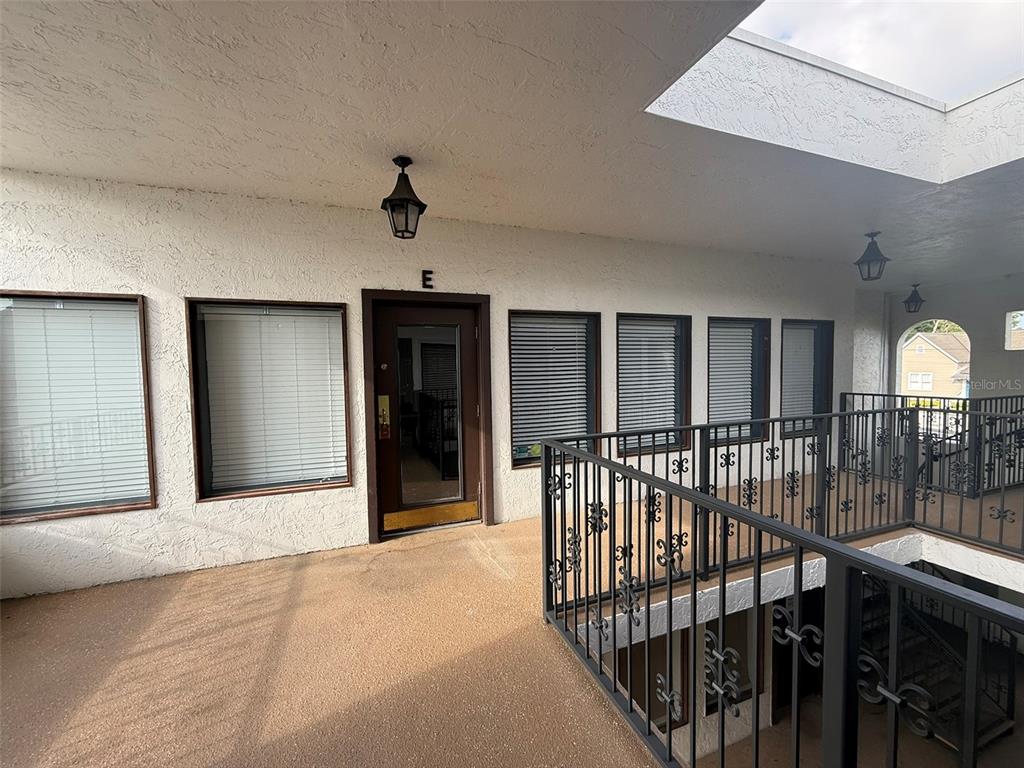 An exterior walkway features a brown door labeled E, windows with blinds, and metal railings — 814 E SILVER SPRINGS BOULEVARD UNIT E, OCALA, FL