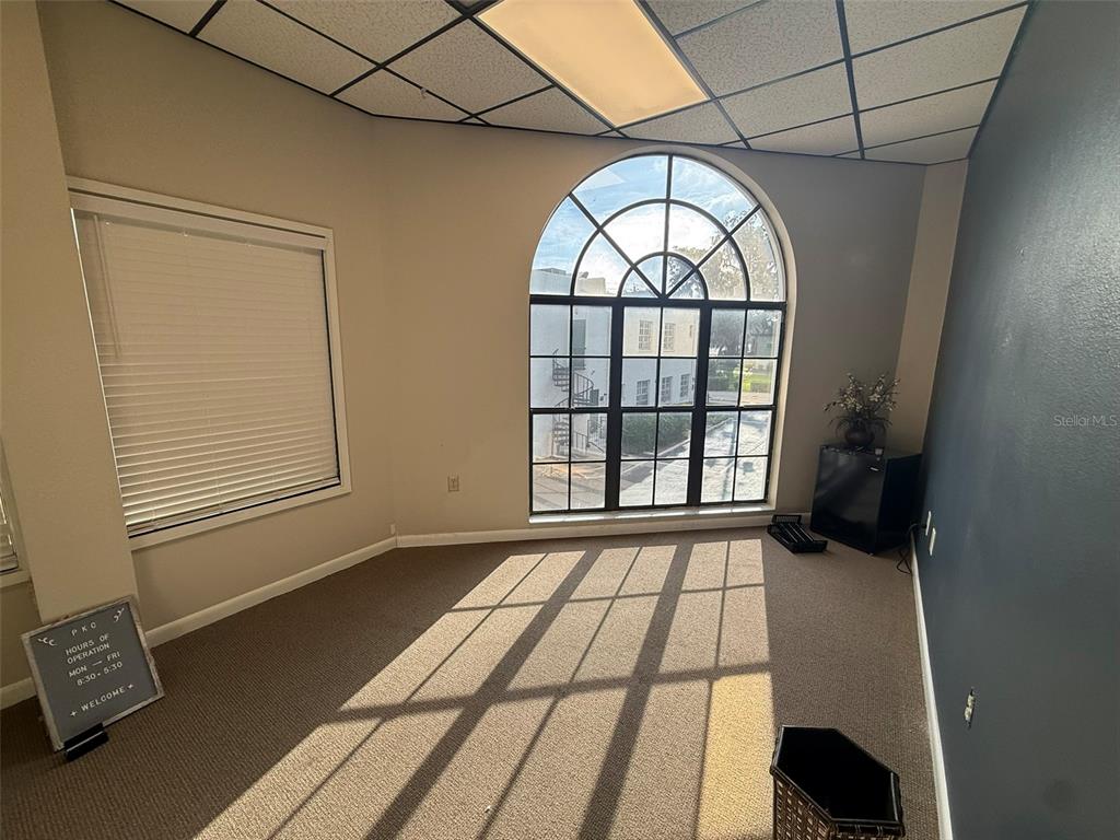 An office space features a large arched window, beige carpet, and a drop ceiling — 814 E SILVER SPRINGS BOULEVARD UNIT E, OCALA, FL