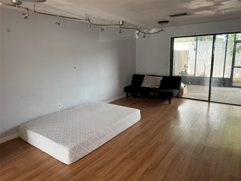An unfurnished room features wood-look flooring, a white mattress, a black futon, and track lighting — 2811 S PINES DRIVE UNIT 18, LARGO, FL