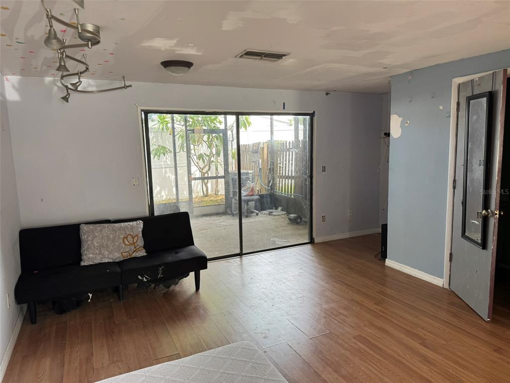 A living room with wood-look flooring, a black futon, and sliding glass doors to a patio — 2811 S PINES DRIVE UNIT 18, LARGO, FL