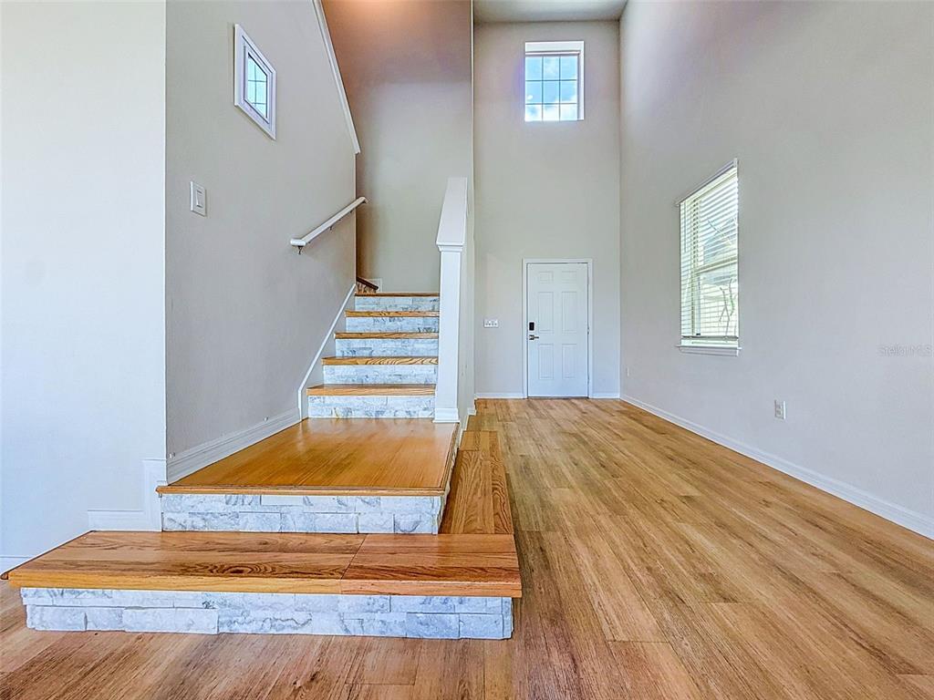 An entryway features a high ceiling, wood flooring, and a staircase with stone-faced risers — 11415 GREEN HARVEST DRIVE, RIVERVIEW, FL