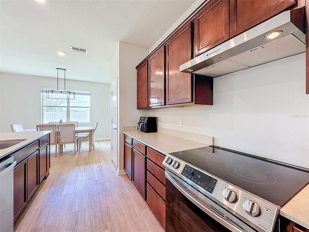A kitchen with dark wood cabinets, stainless steel appliances, and a dining area in view — 11415 GREEN HARVEST DRIVE, RIVERVIEW, FL