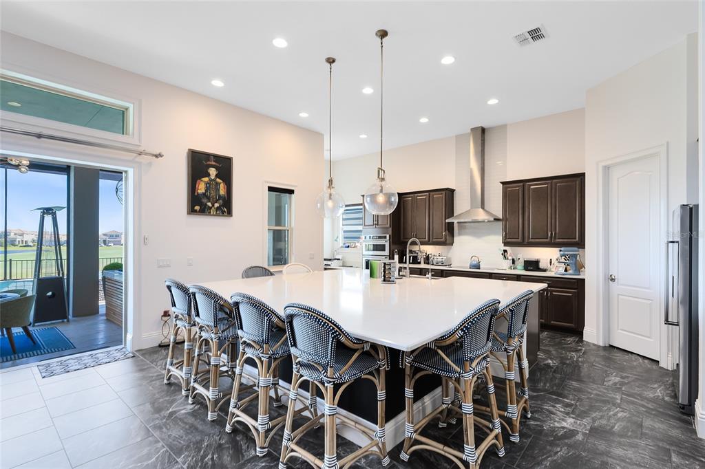 A kitchen features a large white island with woven bar stools and dark cabinetry — 13319 ALDERLEY DRIVE, ORLANDO, FL