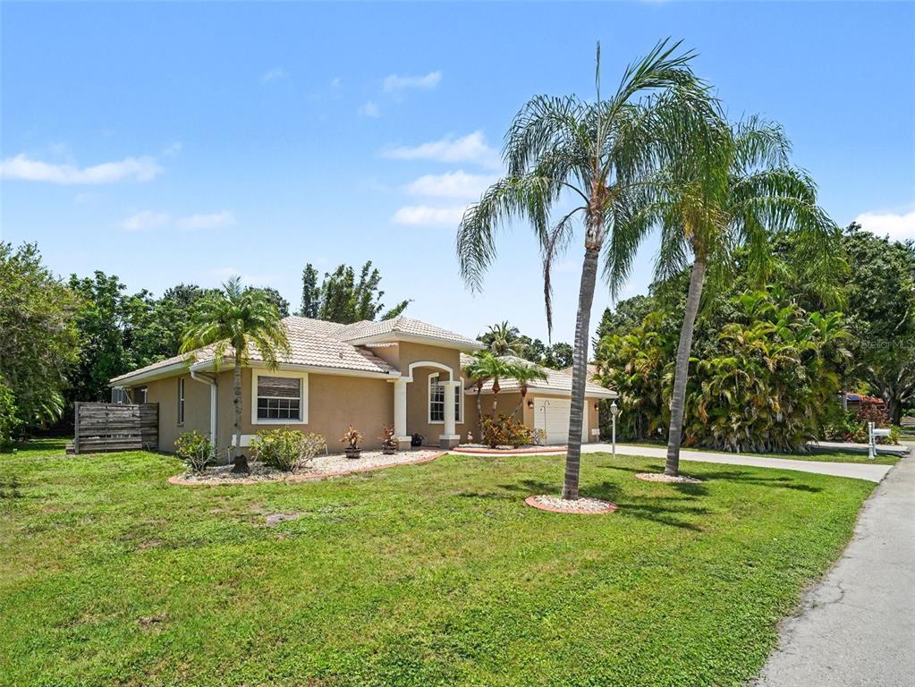 A tan, single-story house with a tile roof and palm trees in the front yard — 4049 GIANNINI LANE, SARASOTA, FL