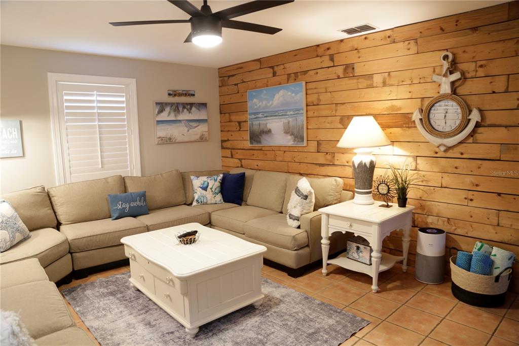 A living room features a beige sectional sofa, a white coffee table, and wood-paneled walls — 1999 N BETTY LANE, CLEARWATER, FL