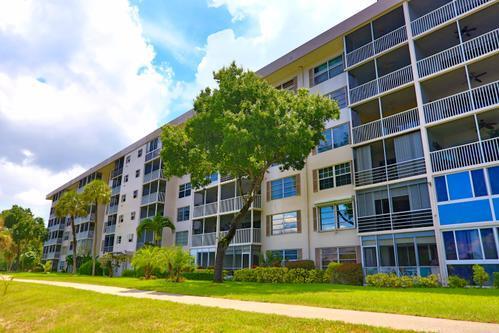 A multi-story apartment building with screened balconies sits next to a grassy lawn and trees — 2801 N Palm Aire Drive # 405, Pompano Beach FL 33069, POMPANO BEACH, FL