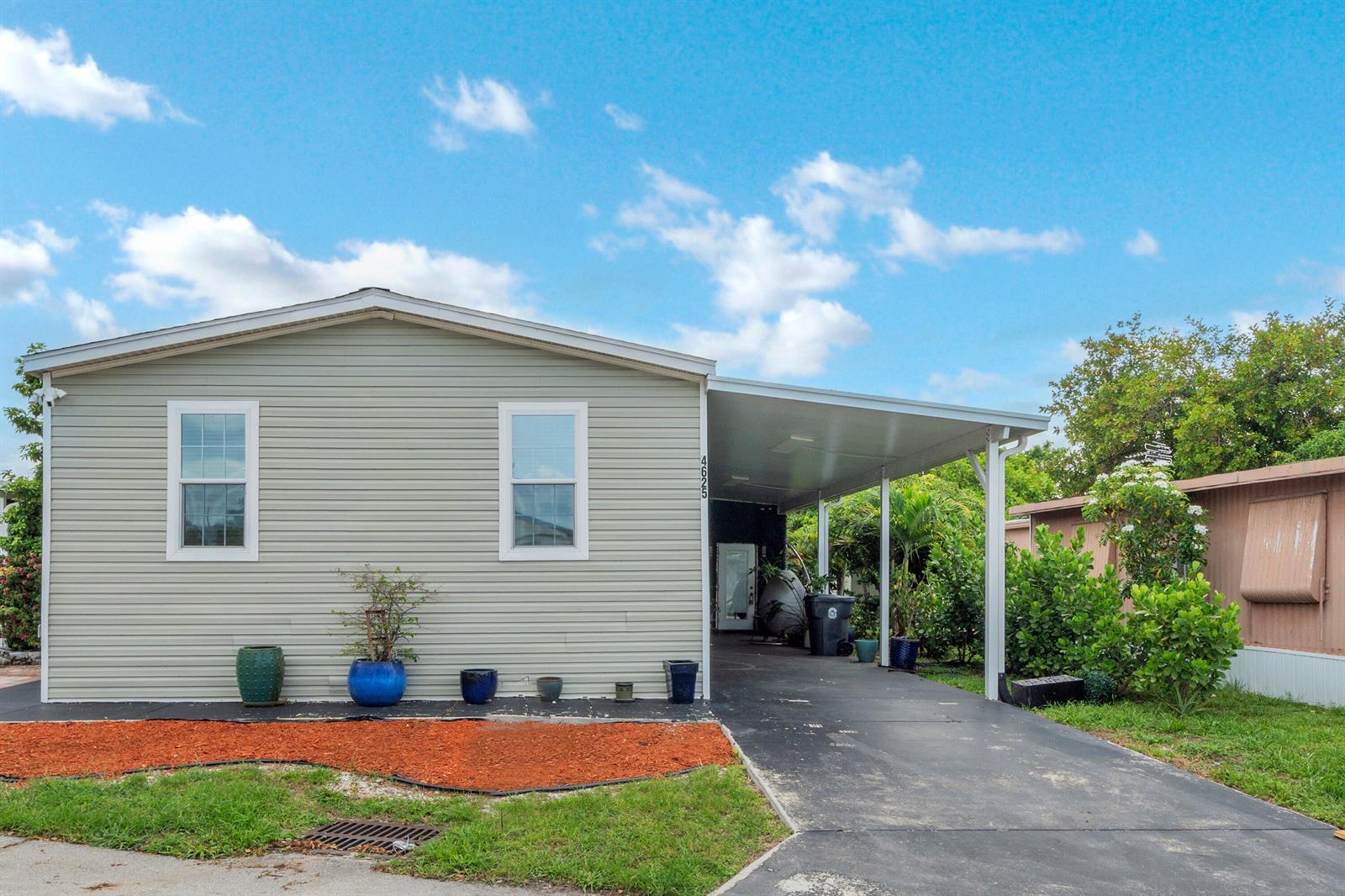 A light green mobile home features a carport, a paved driveway, and a small garden bed — 4625 Jill Place, FL 33463, FL