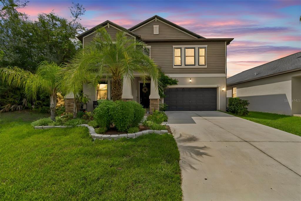 A two-story house with a gray garage, tan siding, and a palm tree in front — 11002 LITTLE BLUE HERON DRIVE, RIVERVIEW, FL