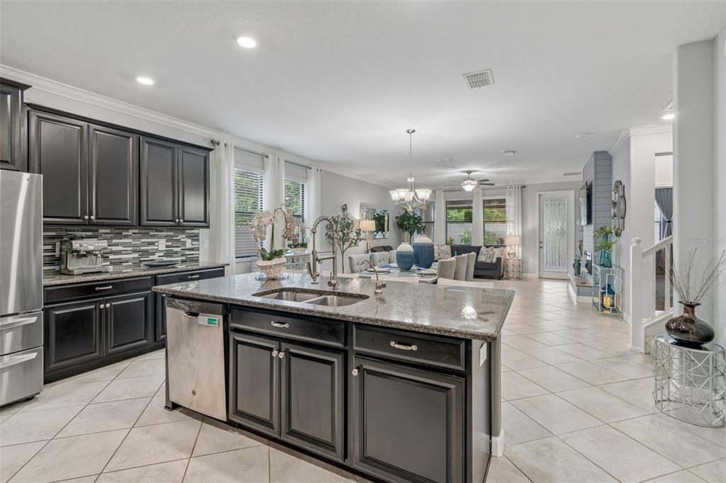 A kitchen with dark cabinets and a granite island overlooks an open-concept dining and living area — 11002 LITTLE BLUE HERON DRIVE, RIVERVIEW, FL
