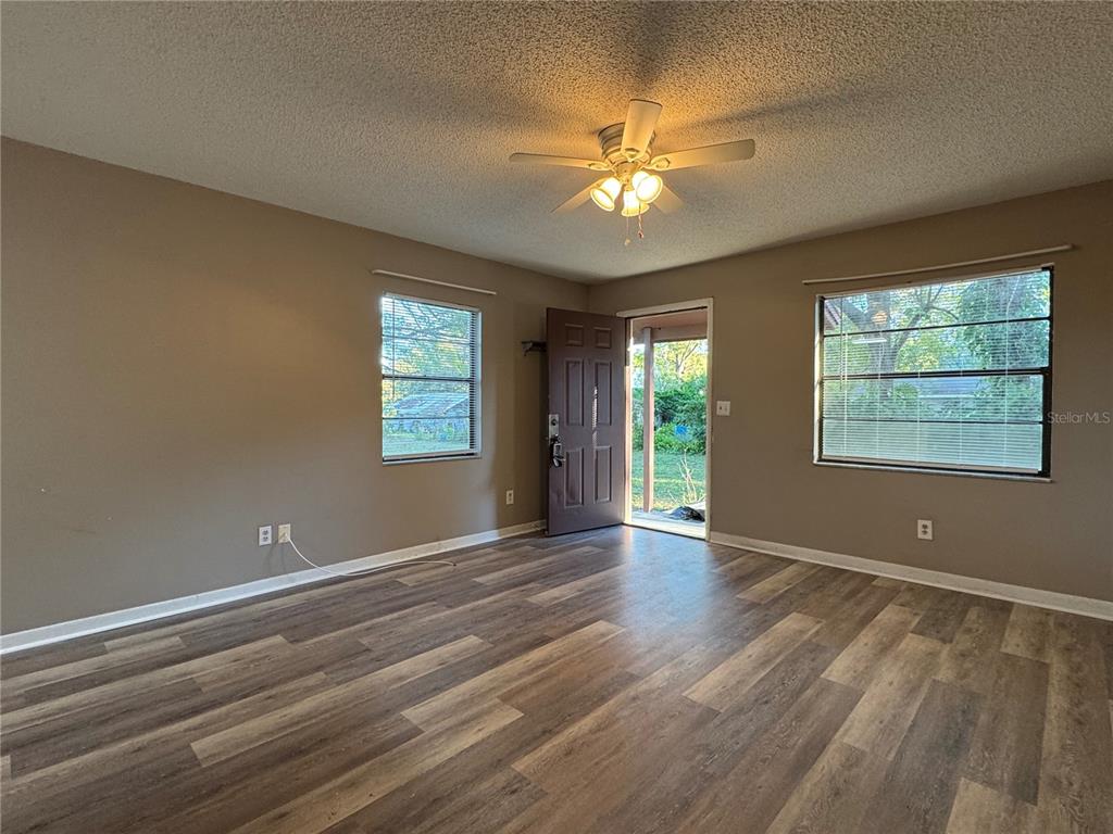 An empty living room features brown walls, wood-look flooring, a ceiling fan, and an open door — 5619 PEACH AVENUE, SEFFNER, FL