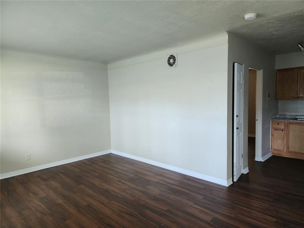 An empty living room features dark wood-look flooring, light-colored walls, and an adjacent kitchen area — 2219 HIGHLAND STREET UNIT 3, ST PETERSBURG, FL