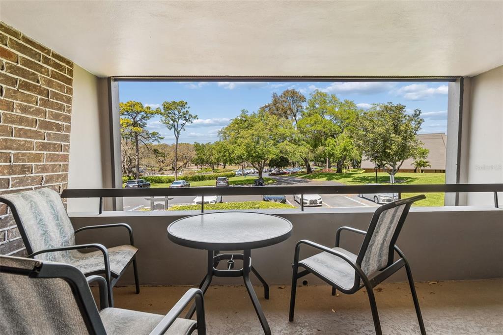 A balcony with a small table and chairs overlooks a parking lot and green trees — 36750 US HIGHWAY 19 N UNIT 22208, PALM HARBOR, FL