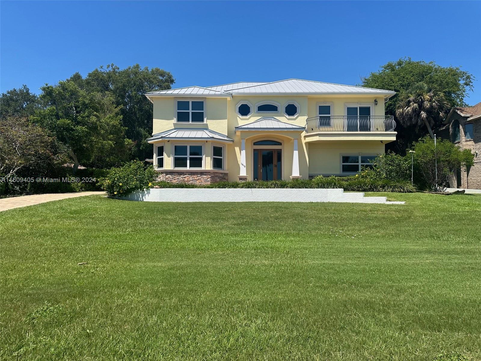A two-story yellow house with a metal roof and a front balcony sits on grass — 1613 N Indian River Drive, Cocoa FL 32922, COCOA, FL
