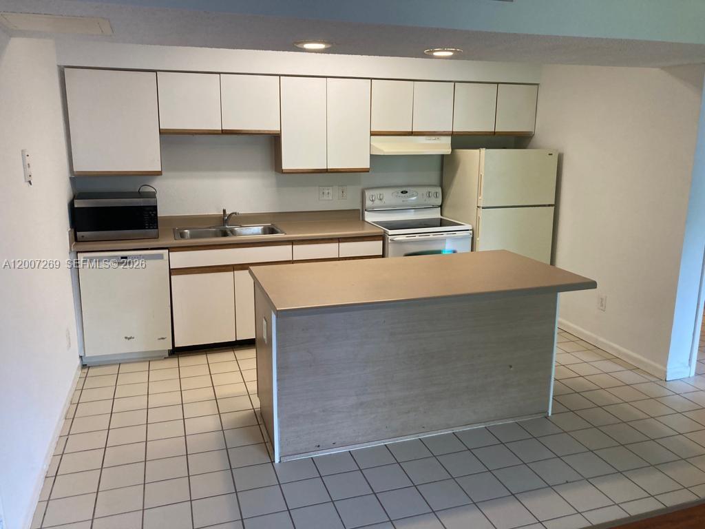 A kitchen features white cabinets, a central island, a double sink, and white tile flooring — 3985 W Mcnab Rd # A111, Pompano Beach FL 33069, POMPANO BEACH, FL