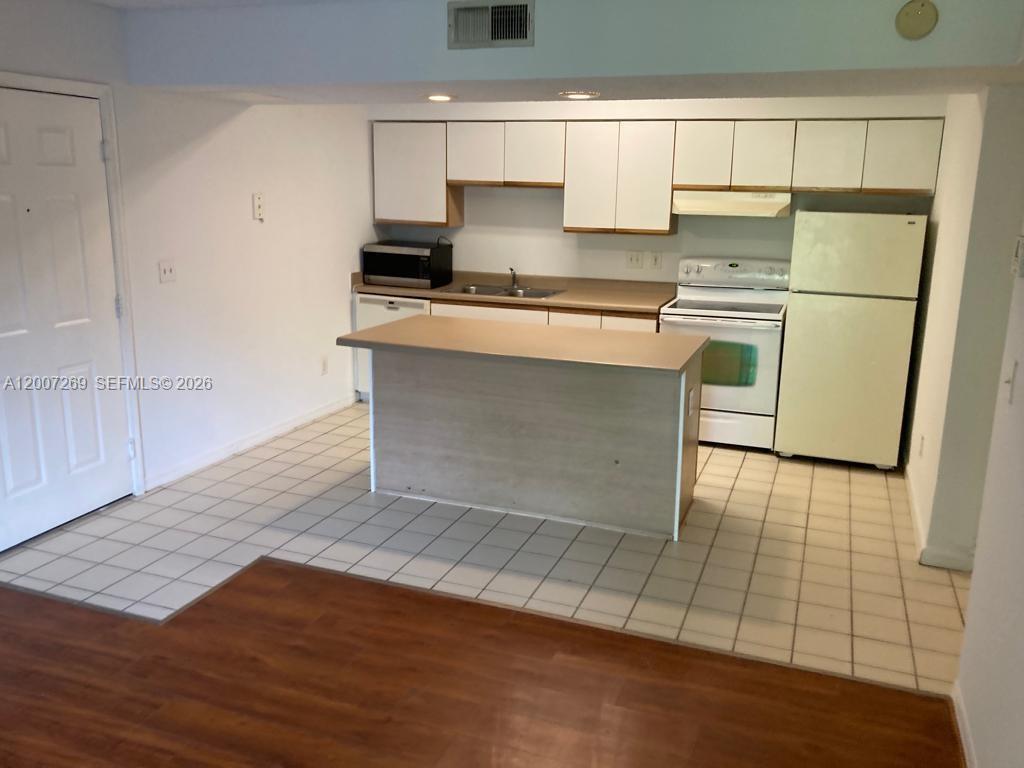A kitchen features white cabinets, a central island, a white stove, and a refrigerator — 3985 W Mcnab Rd # A111, Pompano Beach FL 33069, POMPANO BEACH, FL