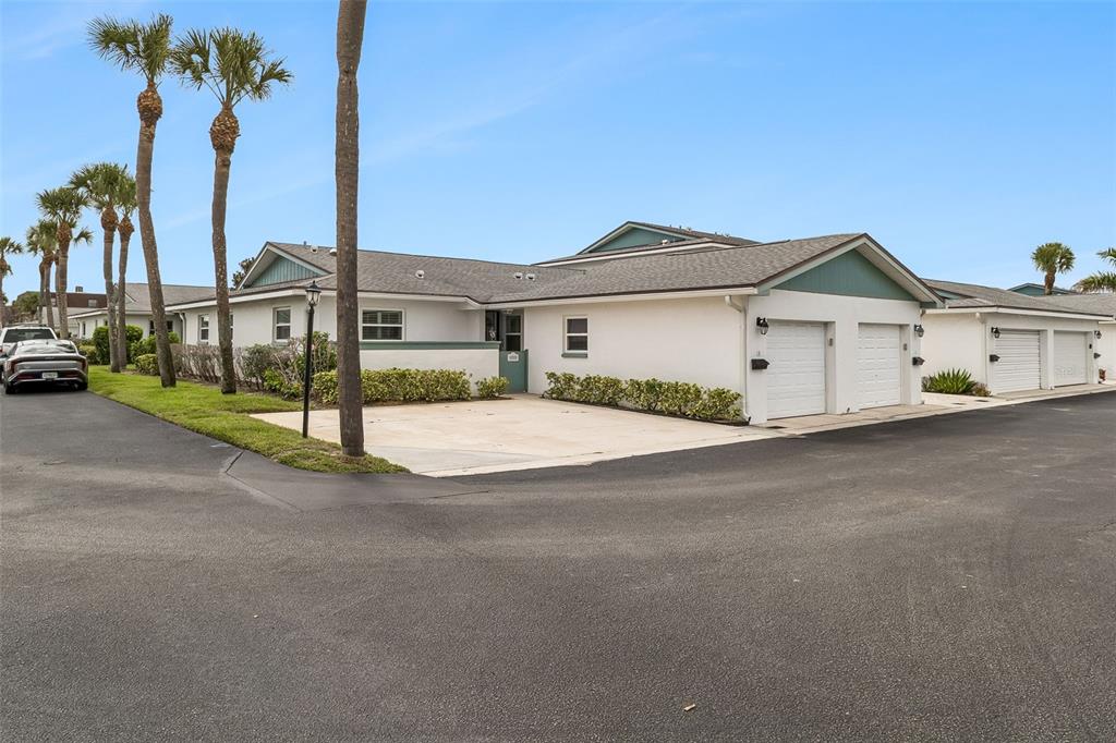 A white single-story house features a two-car garage, a paved driveway, and several palm trees — 290 PARADISE BOULEVARD UNIT 13, MELBOURNE, FL
