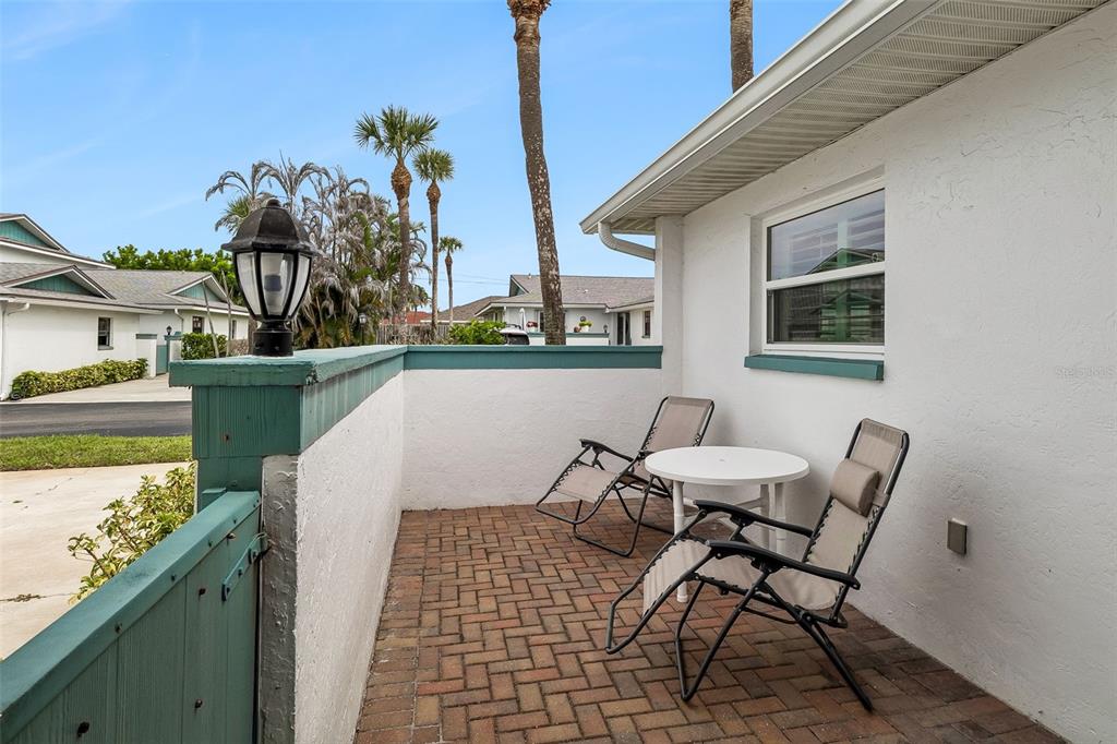 A small brick patio features two folding chairs, a round table, and a low wall — 290 PARADISE BOULEVARD UNIT 13, MELBOURNE, FL