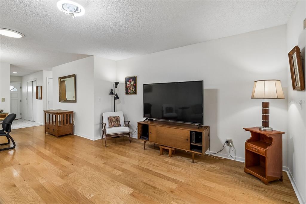 A living room features hardwood floors, a television on a wooden console, and a floor lamp — 290 PARADISE BOULEVARD UNIT 13, MELBOURNE, FL