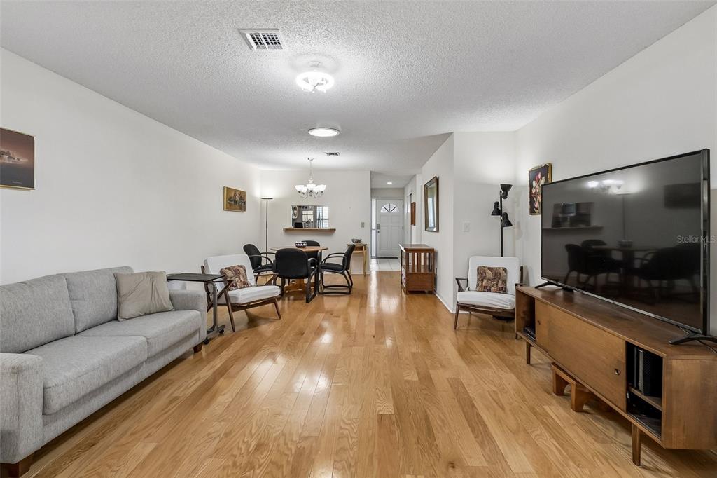 A living room with hardwood floors, a grey sofa, a television, and a dining area — 290 PARADISE BOULEVARD UNIT 13, MELBOURNE, FL