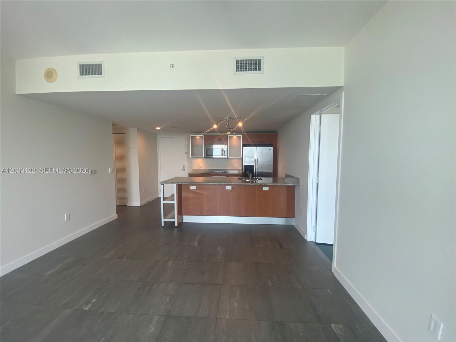 An open-concept kitchen features wood cabinetry, a granite island, and dark tile flooring — 185 SW 7th St # 4206, Miami FL 33130, MIAMI, FL