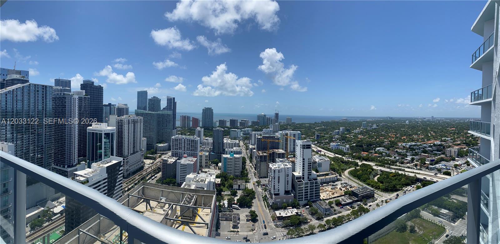 A high-angle view from a balcony overlooks a dense city skyline and distant ocean — 185 SW 7th St # 4206, Miami FL 33130, MIAMI, FL