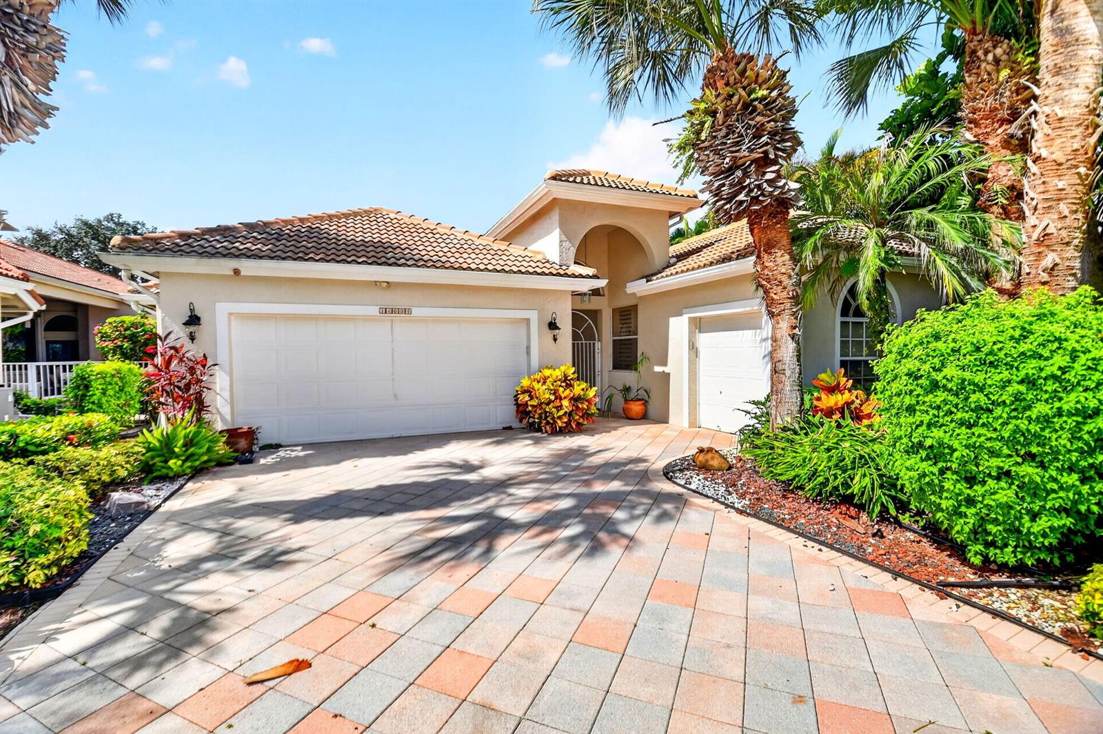 A beige house with a tiled roof, two garage doors, and a paved driveway — 10694 Greenbriar Villa Drive, Lake Worth FL 33449, LAKE WORTH, FL
