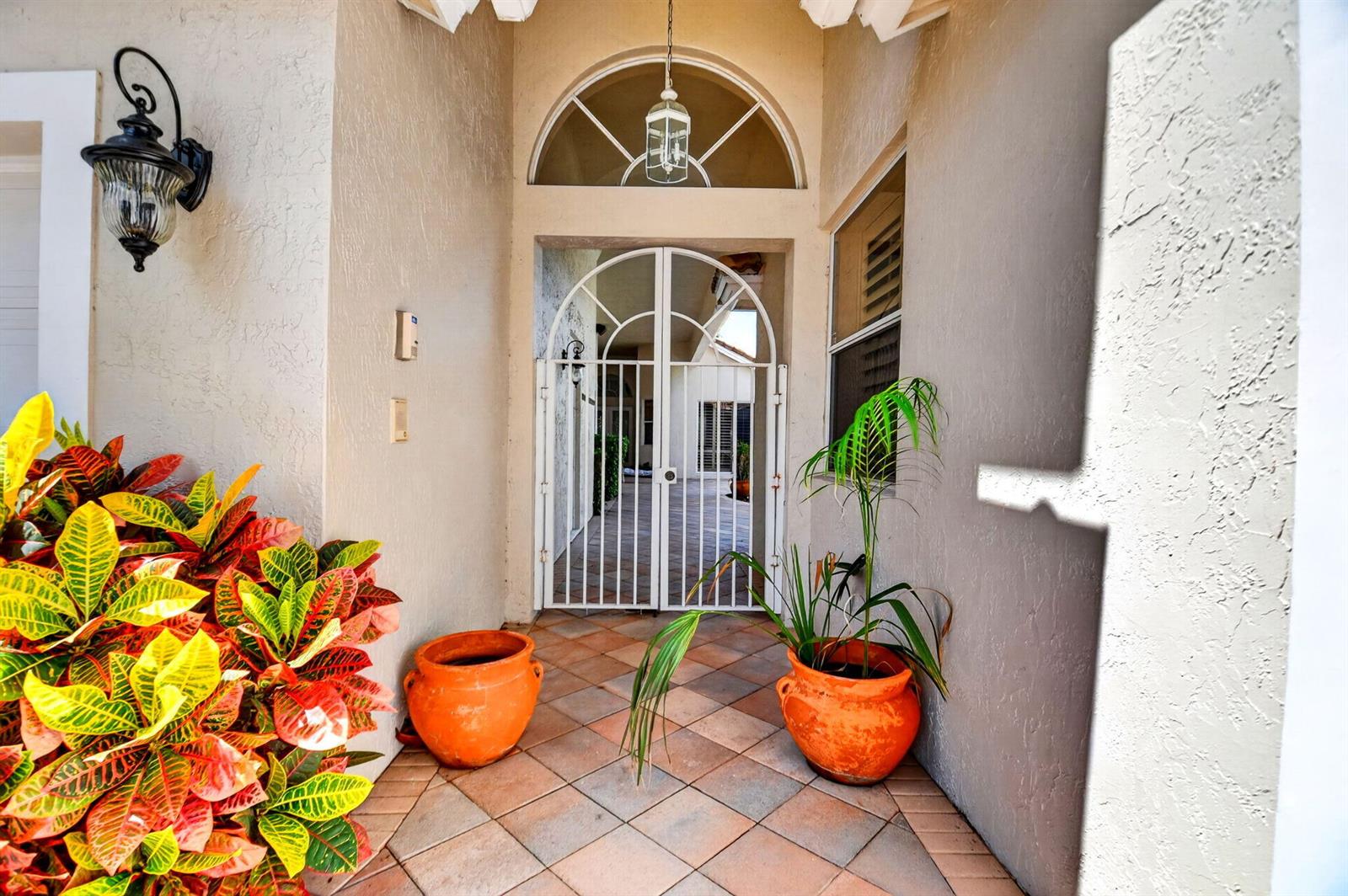 An outdoor entryway features a white metal gate, terracotta pots, and a tiled floor — 10694 Greenbriar Villa Drive, Lake Worth FL 33449, LAKE WORTH, FL