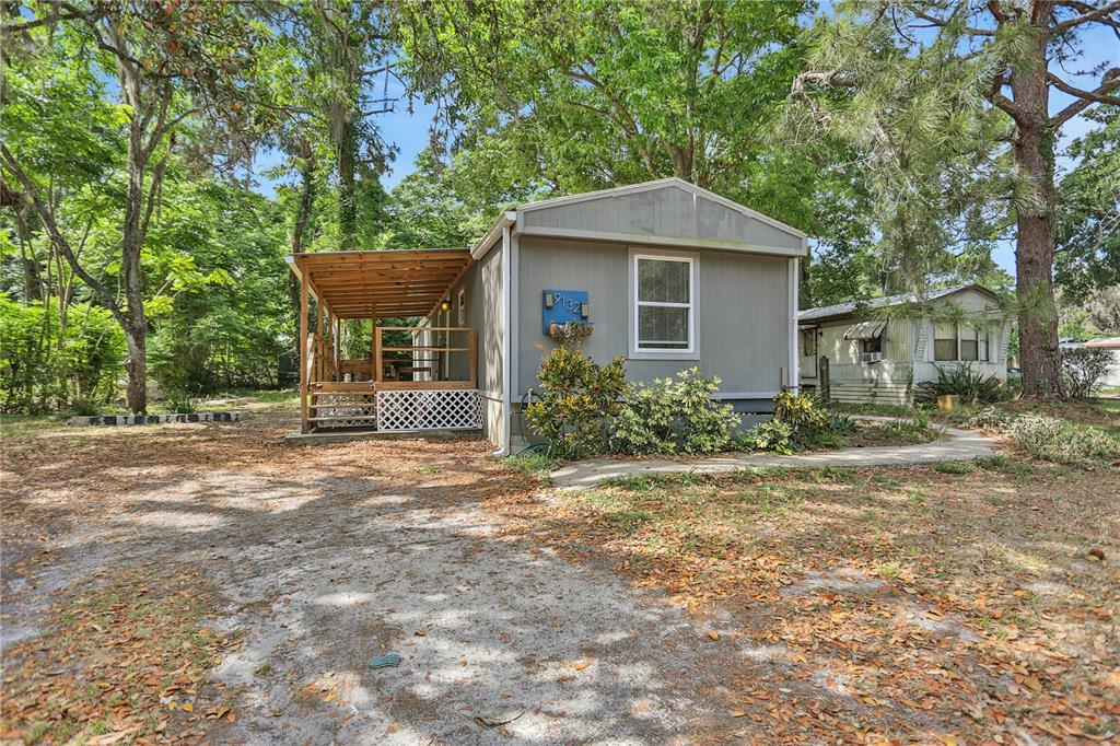 A gray mobile home with a wooden porch and lattice skirting sits on a dirt lot — 9132 MANGO STREET, NEW PORT RICHEY, FL