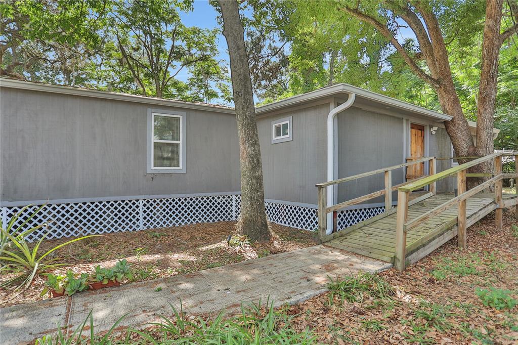 A gray mobile home features a wooden wheelchair ramp leading to an entrance door — 9132 MANGO STREET, NEW PORT RICHEY, FL