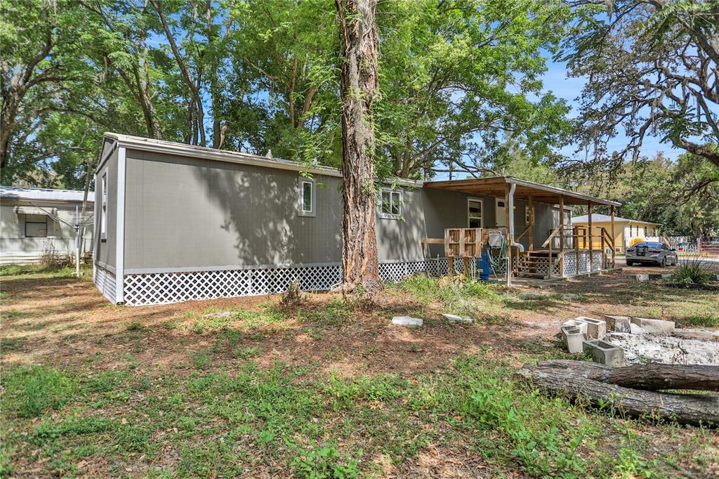 A single-story mobile home with a wooden porch and white lattice skirting sits among trees — 9132 MANGO STREET, NEW PORT RICHEY, FL