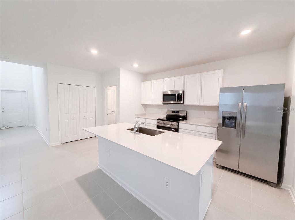 A modern kitchen features white cabinets, stainless steel appliances, and a central island with sink — 5420 MEADOW WALK DRIVE, DAVENPORT, FL