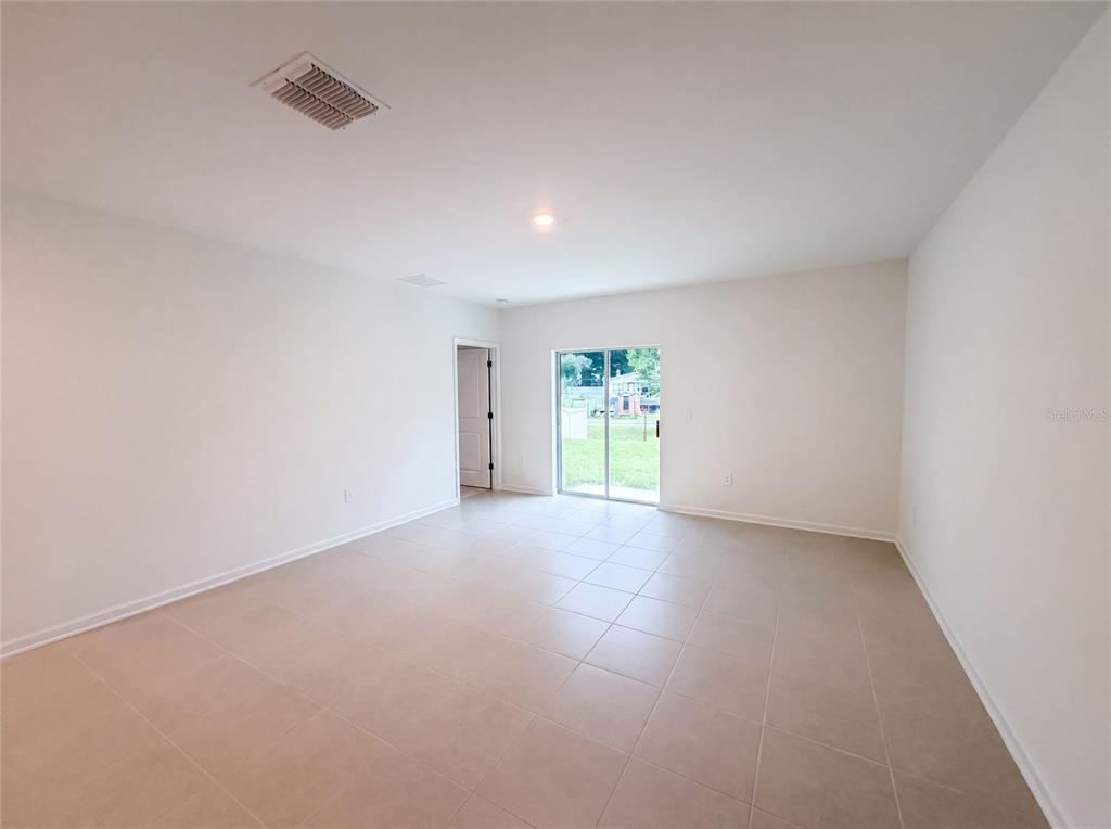 A bright, empty room features light-colored tile flooring, white walls, and a sliding glass door — 5420 MEADOW WALK DRIVE, DAVENPORT, FL